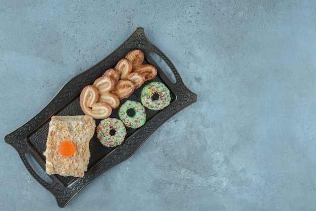 Disposizione di dessert con biscotti a fiocchi, una fetta di torta, ciambella e su un vassoio decorato su una superficie di marmo