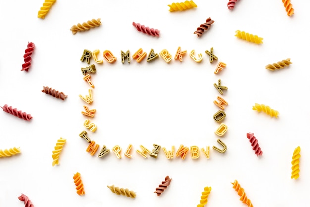 Disposizione di fusilli colorati crudi e cornice di pasta alfabeto