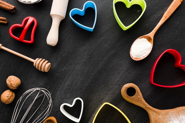 Disposizione piana delle forme colorate del cuore con delle forme colorate del cuore con gli utensili della cucina