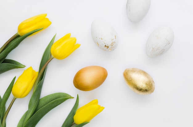 Disposizione piana delle uova di Pasqua dorate con i fiori