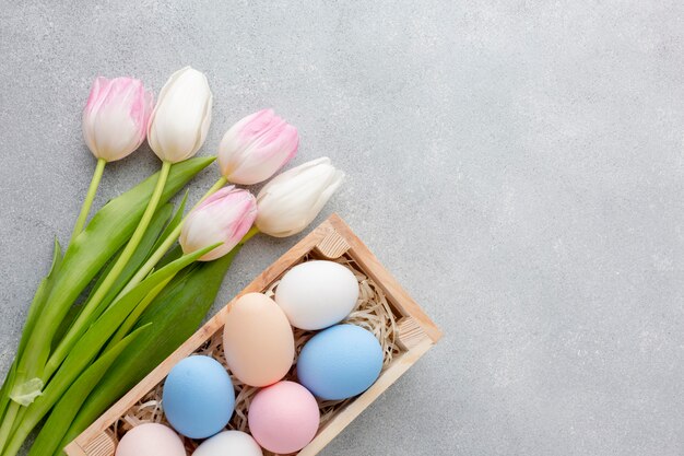 Disposizione piana delle uova di Pasqua variopinte in scatola con i tulipani e lo spazio della copia