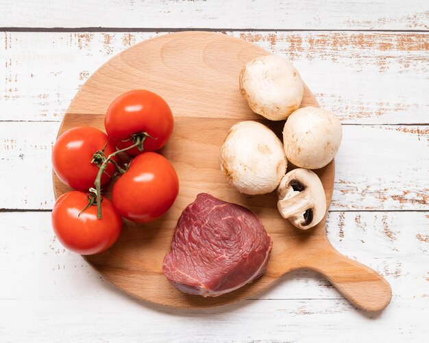Disposizione piana di carne e verdure sulla tavola di legno
