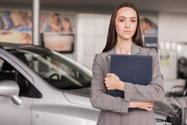 Distogliere lo sguardo femminile sicuro del commerciante di automobile