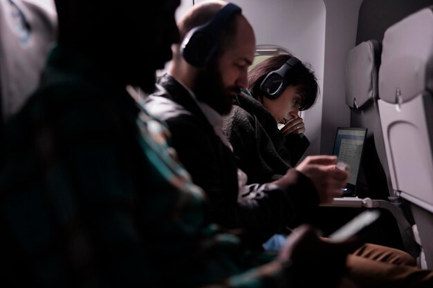 Diverse persone che viaggiano in aereo e utilizzano il laptop durante il volo internazionale di vacanza. Uomini e donne in attesa di arrivare a destinazione di vacanza, volando con il servizio aereo in aereo.