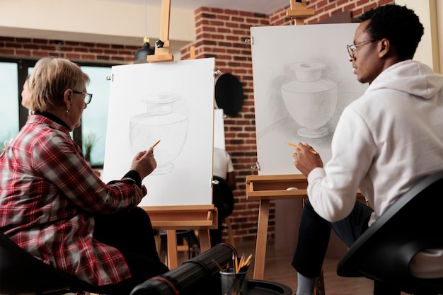 Diverse persone di diverse generazioni disegnano su tela e parlano durante la lezione di arte creativa in uno studio moderno.