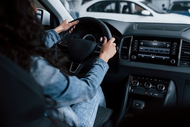 Diversi pulsanti e manopole. Ragazza carina con capelli neri, cercando la sua macchina costosa nuova di zecca nel salone dell'automobile