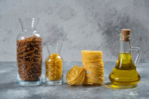 Diversi tipi di maccheroni crudi con una bottiglia di olio di vetro.