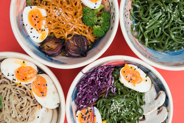 Diversi tipi di pasta con uova; alghe e insalata nella ciotola sul fondale rosso