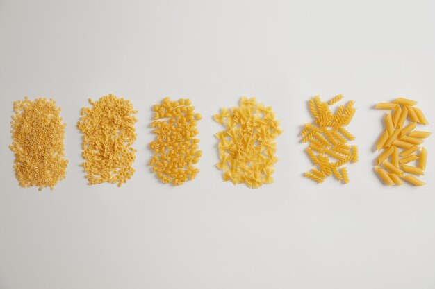 Diversi tipi di pasta italiana su sfondo bianco. Farfalle, fusillini, penne, stelline, chiocciole crude crude. Tipi tradizionali. Sfondo del menu. Concetto di cibo e nutrizione. Cucina casalinga