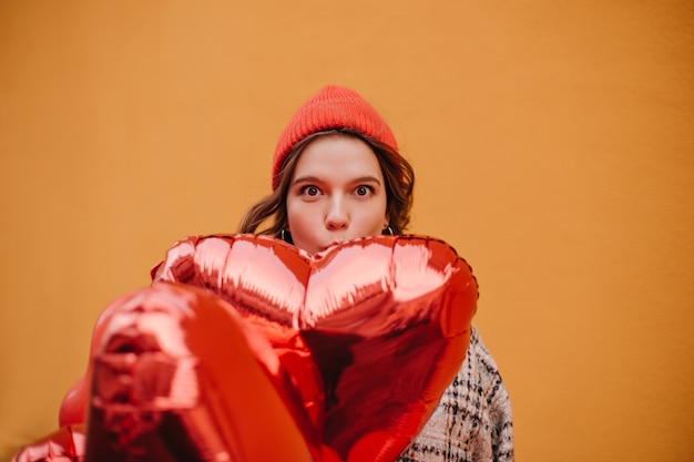 Divertente giovane donna con cappello rosso copre parte del viso con un enorme palloncino lucido