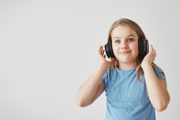 Divertente ragazza allegra con i capelli chiari e gli occhi azzurri, indossando le cuffie. con espressione scioccata dopo che la musica ad alto volume inizia improvvisamente a suonare