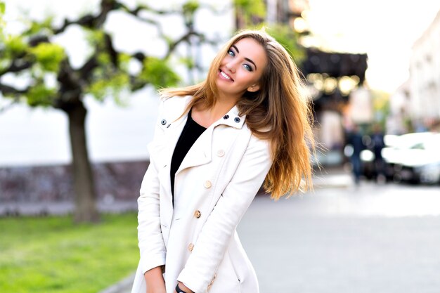 Divertente ritratto di felice ragazza bionda, facendo facce buffe e mostrando la lingua per strada, tempo di autunno, resto in città.