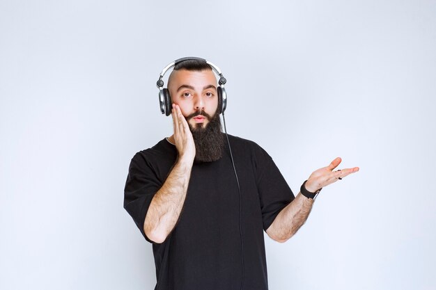 DJ con la barba che indossa le cuffie, mostra il lato destro e rimane sorpreso.