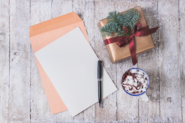 Documento in bianco con una penna a sfera e la tazza con marshmallow e un regalo