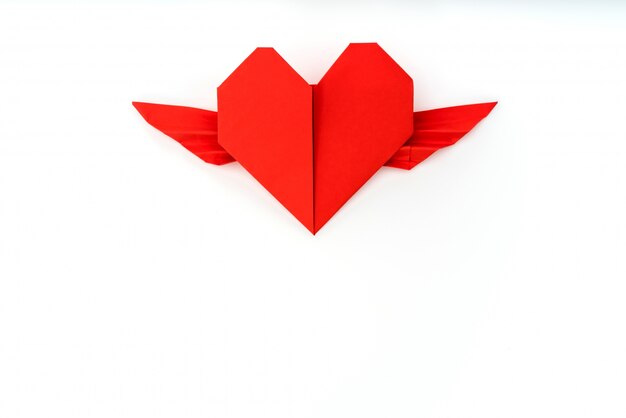 Documento rosso cuore origami con le ali su sfondo bianco.
