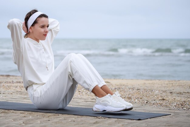Dolce atleta femminile che fa addominali sul materassino in spiaggia Foto di alta qualità