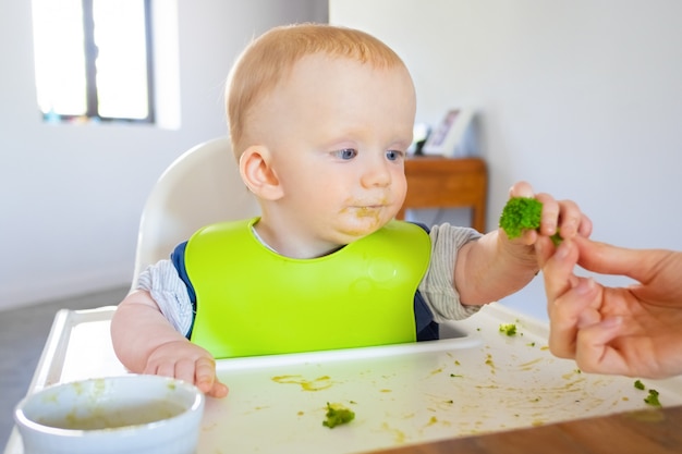Dolce bambino in bavaglino prendendo broccoli pezzo dalla mamma
