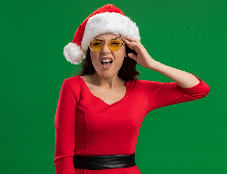 Foto gratuito dolorante giovane bella ragazza che indossa santa cappello e occhiali guardando la telecamera toccando la testa soffre di mal di testa isolato su sfondo verde