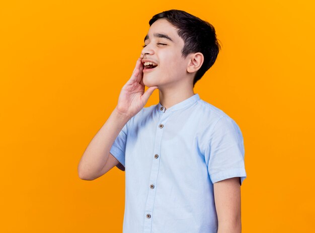Dolorante giovane ragazzo caucasico tenendo la mano sulla guancia con mal di denti isolato su sfondo arancione con copia spazio