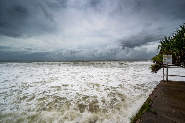 Dolore schiumoso sotto il cielo nuvoloso scuro in Alexandra Headland Beach, Queensland Australia