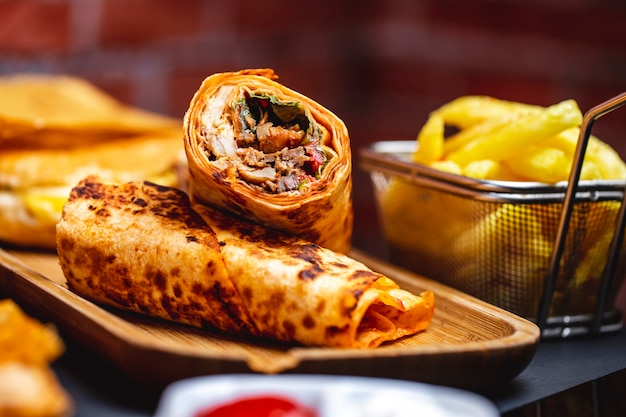 Doner vista laterale con pollo alla griglia verdi lattuga pomodoro e patatine fritte sul tavolo