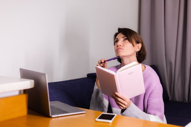 Donna a casa con il taccuino del blocco note pensando ai piani