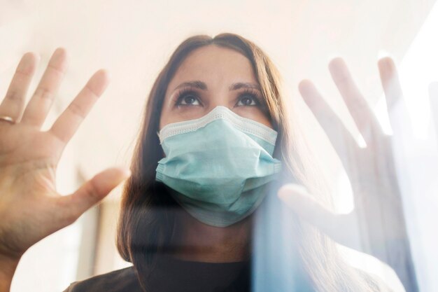 Donna a casa in quarantena con mascherina medica dietro la finestra