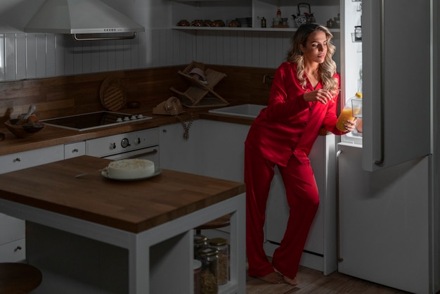 Donna a figura intera che controlla il frigorifero di notte