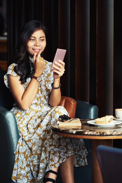 Donna abbastanza asiatica che si siede in caffè e che prende selfie con lo smartphone