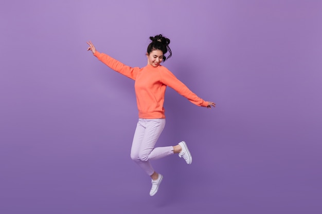 Donna abbastanza asiatica spensierata che salta con il sorriso. Studio shot di divertente donna coreana che balla su sfondo viola.