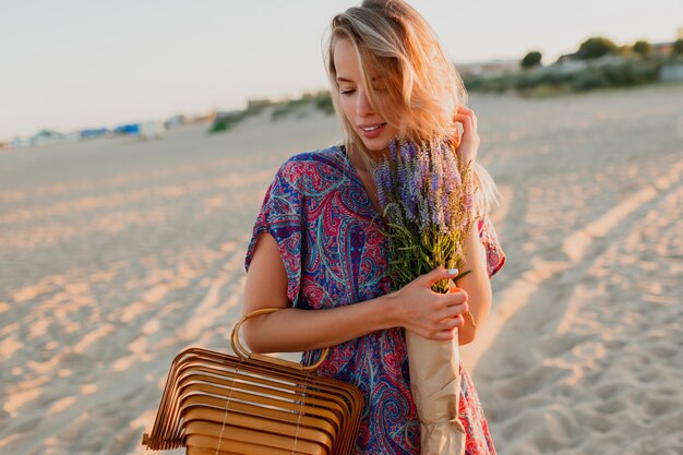 Donna abbastanza bionda con bouquet di lavanda che cammina sulla spiaggia. I colori del tramonto.