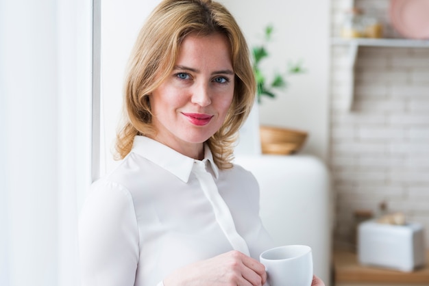 Donna abbastanza bionda di affari che si leva in piedi con la tazza di caffè