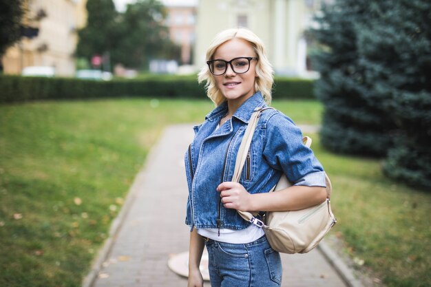 Donna abbastanza bionda in ritratto di occhiali in città che indossa jeans suite al mattino