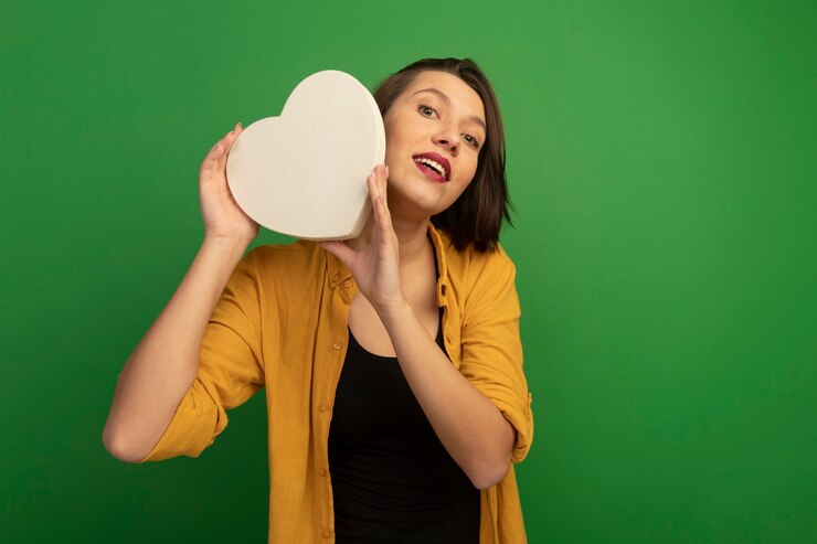 Foto gratuito donna abbastanza caucasica emozionante che tiene forma del cuore sul verde