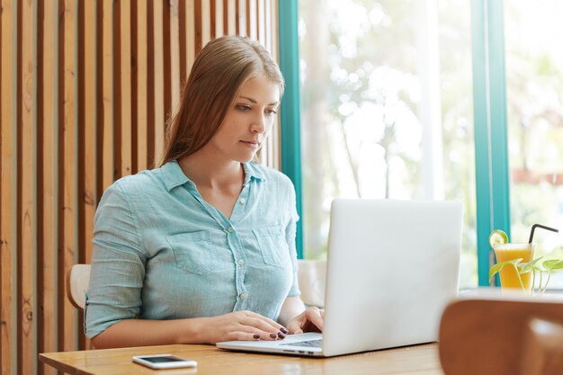 Donna abbastanza giovane con capelli lunghi che si siede nella caffetteria con il computer portatile