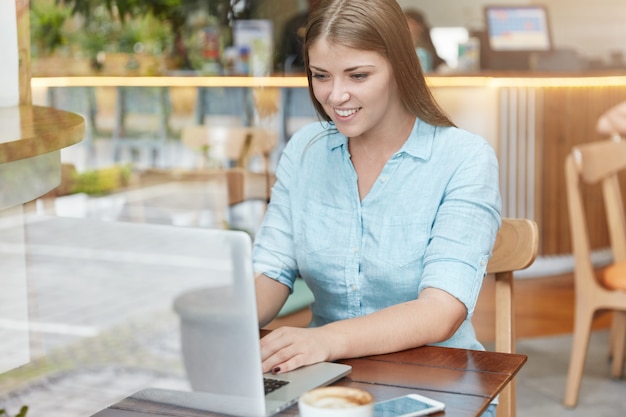 Donna abbastanza giovane con capelli lunghi che si siede nella caffetteria con il computer portatile