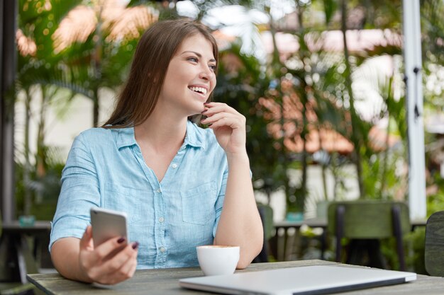 Donna abbastanza giovane con capelli lunghi che si siede nella caffetteria con il computer portatile