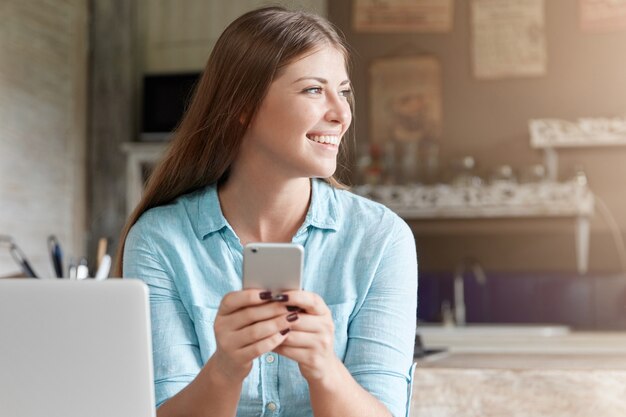 Donna abbastanza giovane con capelli lunghi che si siede nella caffetteria con il computer portatile