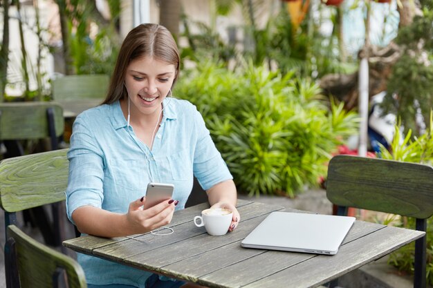 Donna abbastanza giovane con capelli lunghi che si siede nella caffetteria con il telefono