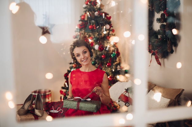 Donna abbastanza sorridente che si siede nella sua camera da letto con il regalo di Natale