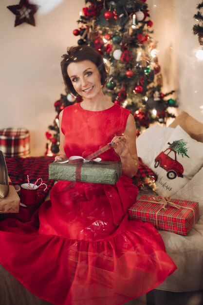 Donna abbastanza sorridente che si siede nella sua camera da letto con il regalo di Natale