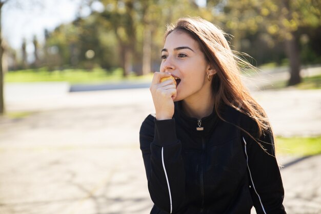 Donna abbastanza sportiva positiva che mangia mela nella sosta della città