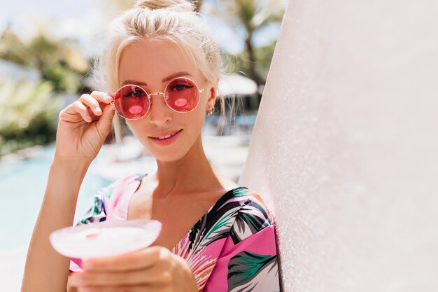 Donna abbronzata alla moda che tocca i suoi occhiali da sole rosa