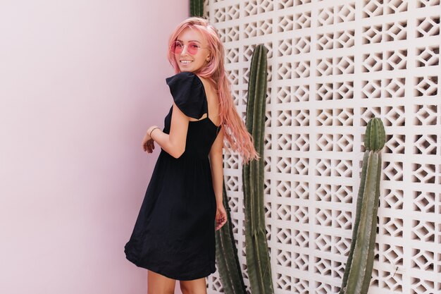 donna abbronzata con i capelli rosa sorridente accanto a cactus.