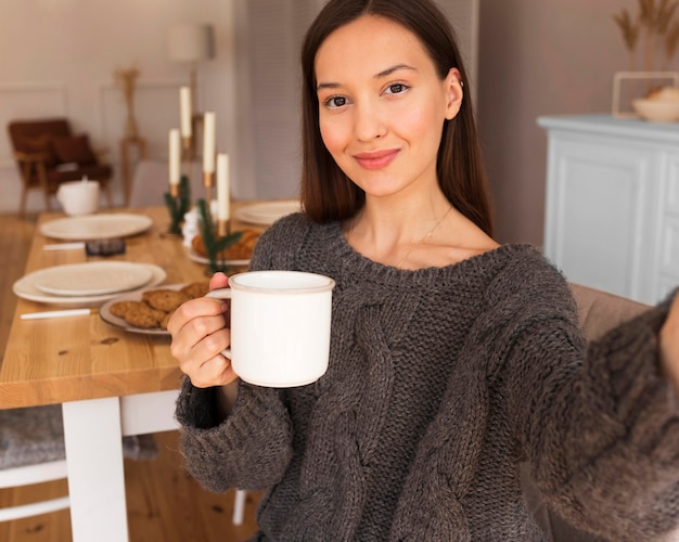 Donna accogliente che tiene la tazza e che prende i selfie