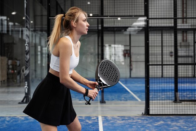 Donna adatta di vista laterale che gioca a paddle tennis