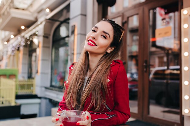 Donna adorabile con trucco alla moda che ride mentre beve il tè sullo spazio della via