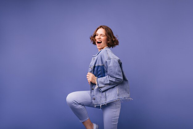 Donna adorabile positiva che salta e che ride. Adorabile modello femminile in giacca di jeans oversize che balla.