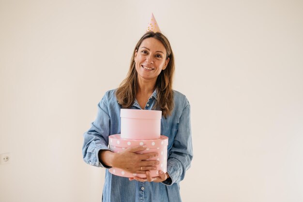 Donna adulta caucasica sorridente in camicia che tiene scatola regalo rosa isolata su sfondo bianco. Piacevole concetto di sorpresa