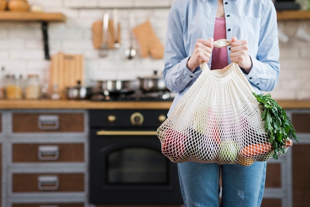 Donna adulta che tiene borsa riutilizzabile con verdure biologiche